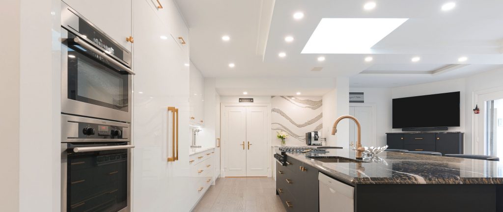 A photorealistic depiction of a contemporary kitchen. Stainless steel appliances, including a refrigerator, oven, and dishwasher, line the walls, their surfaces catching the sunlight streaming through large windows. A white marble countertop graces the central island and surrounding counters, offset by sleek dark cabinets. A flat-screen TV hangs above the sink, adding a touch of modern convenience.