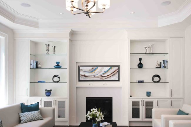 Modern living room with white built-in shelves, fireplace, and abstract art.