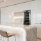 Modern white kitchen with marble island, bar stools, and wine fridge.