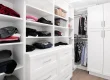 A well-organized white walk-in closet with shelves, drawers, and hanging clothes.