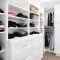 A well-organized white walk-in closet with shelves, drawers, and hanging clothes.