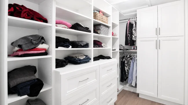 usersFfed afe da afffacdFlibraryFbd fc c bec fbdFWalk inClosetDesign A well-organized white walk-in closet with shelves, drawers, and hanging clothes.