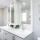 Modern white bathroom vanity with double sinks and a decorative tree wall art.